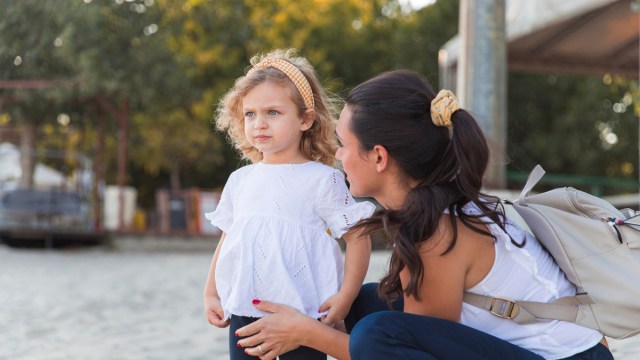 mom crouching beside toddler girl talking to her about something serious