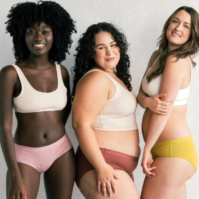 three women standing in sports bras and underwear against a grey backdrop