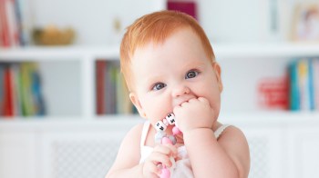 a baby sitting and chewing on a teether for a story on teething tips