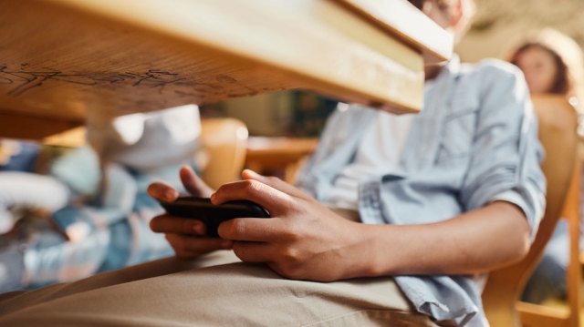 student looking at their phone under their desk