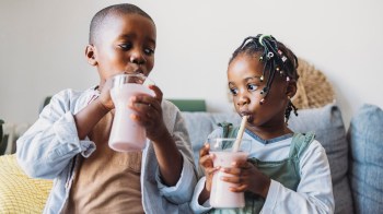 Two kids drinking smoothies for a story on smoothie recipes for kids that help with constipation, the sniffles and more.