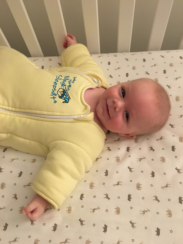 a baby lying in their crib wearing the yellow Baby Merlin's Magic Sleepsuit