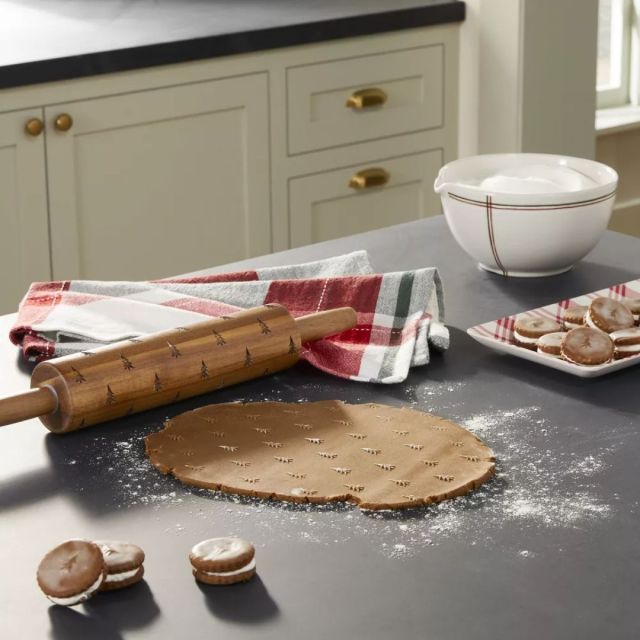 kitchen countertop featuring a rolled out sheet of christmas cookie dough and a christmas tree stamped rolling pin