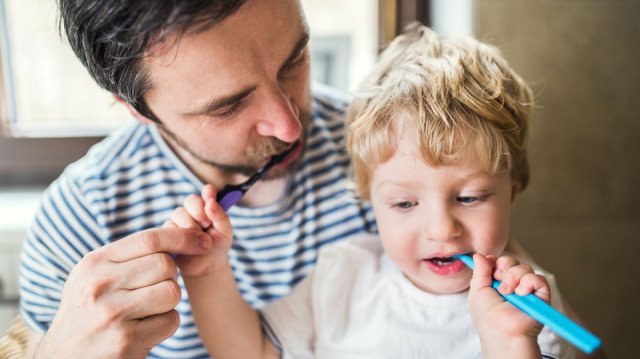 dad and toddler son brushing their teeth