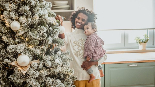 a mom and baby cuddling by the christmas tree for a story on baby's first holiday season