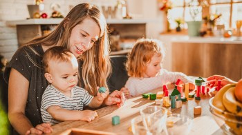 a nanny who is part of a nanny share playing blocks with two kids