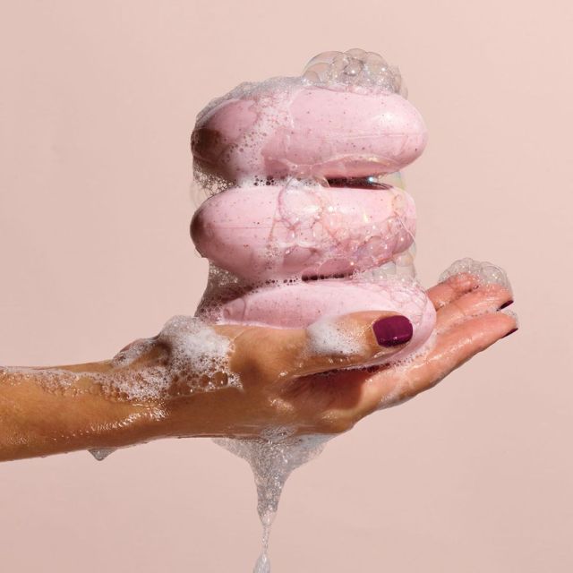hand holding a stack of 3 pink bars of soap with suds