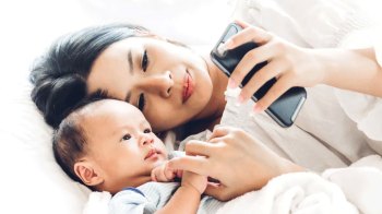 a mom and baby on the bed looking at mom's phone where she's using one of the best baby tracking apps