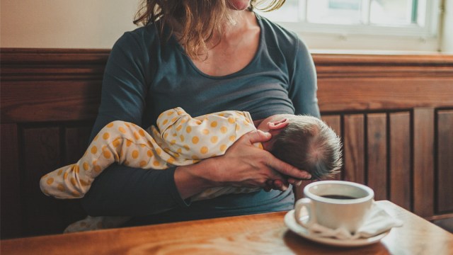 a woman breastfeeding in a coffee shop with a cup of coffee for a story answering the question 'can you drink coffee while breastfeeding?'