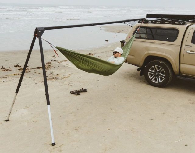 man lounging in a hammock attached to a truck on the beach