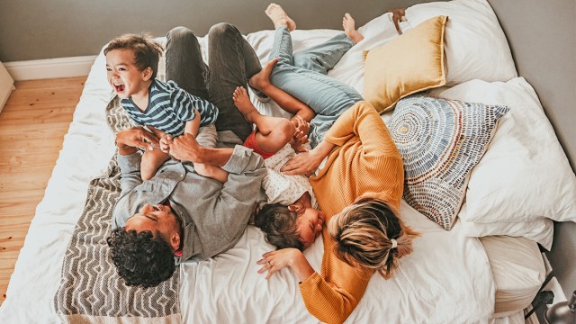 a family playing on the bed for a photoshoot, one of the best family photo ideas with toddlers