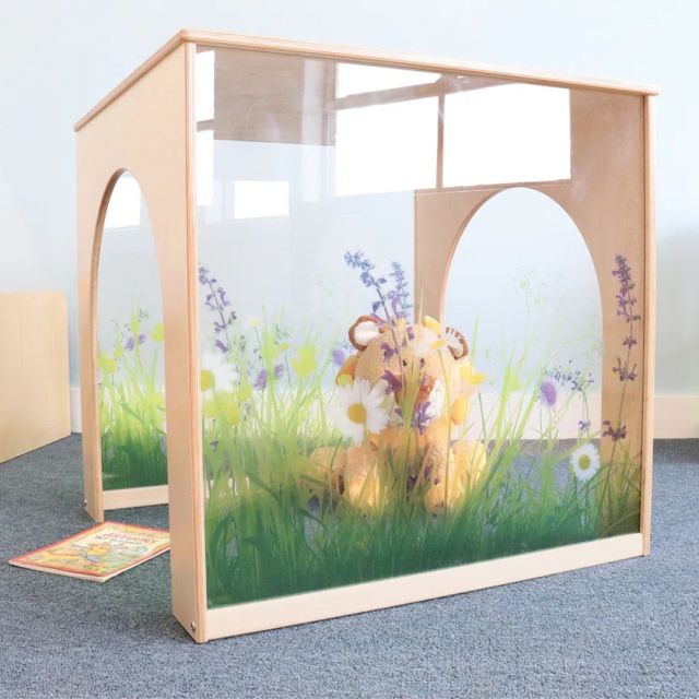 clear playhouse with grass and glowers painted on it sits on a grey carpet in a classroom