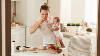 mom eating foods that are good for a postpartum diet while holding baby