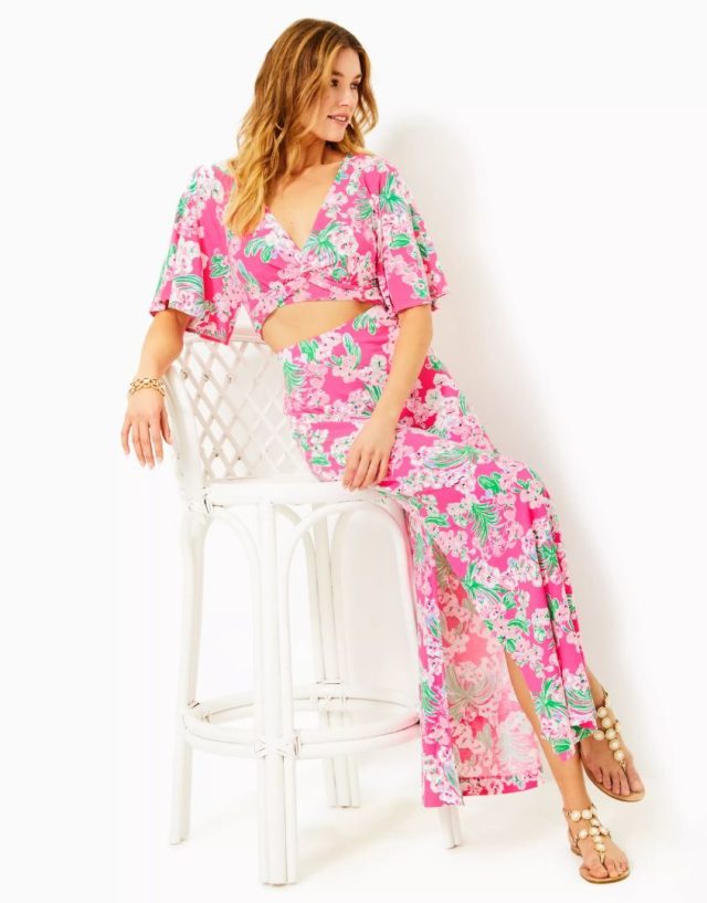 woman perched on white chair wearing pink floral maxi skirt and matching crop top