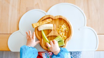 a baby hand grabbing sticks of food off a plate while learning baby-led weaning