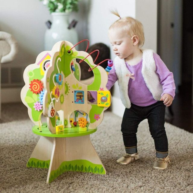 toddler girl in a living room playing with a wooden toy treehouse