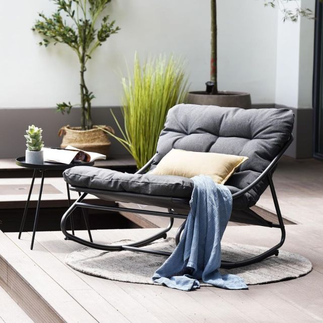 grey cushion outdoor rocking chair on patio with blanket and pillow draped over it