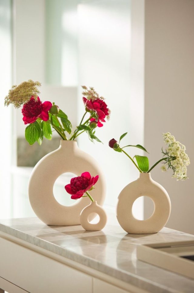 two round vases on a table with white and red flowers