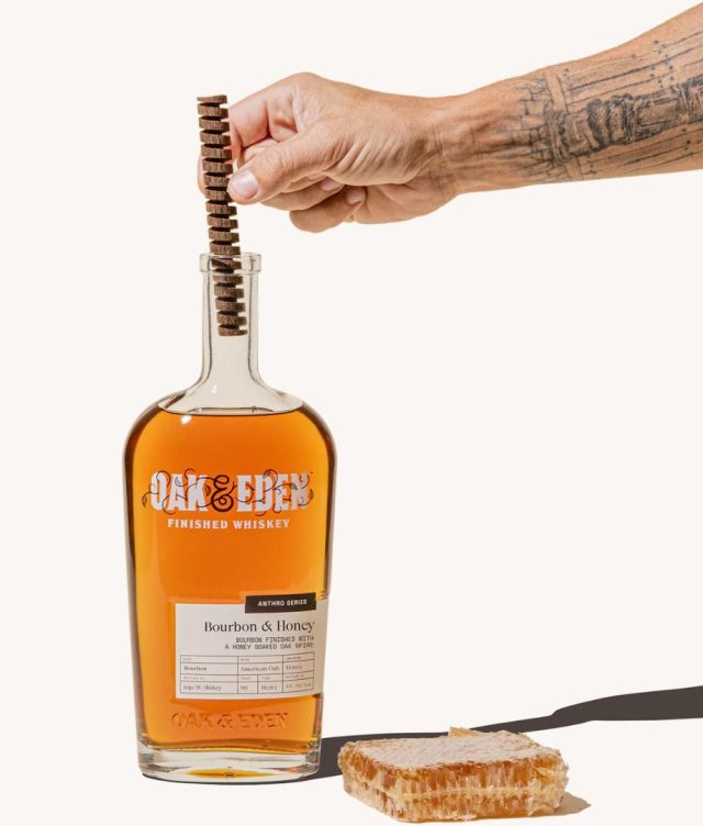 bottle of customized Oak & Eden Whiskey with a hand dropping a wood spire into it