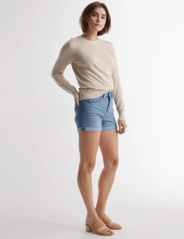 woman standing in tan sweater and denim shorts