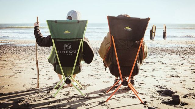 two people sitting in portable chairs on the beachh