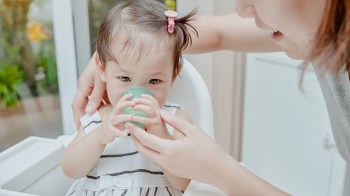 a baby drinking water from a cup for a story on when can babies have water