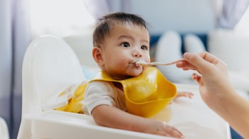 An infant in a yellow bib trying one of the best first foods for baby