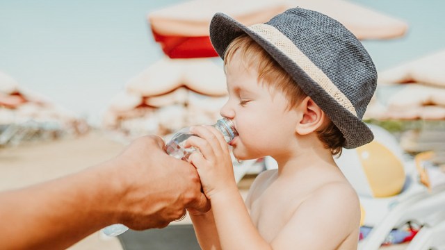 a little boy drinking some water on the beach alongside some hydrating foods like cantaloupe