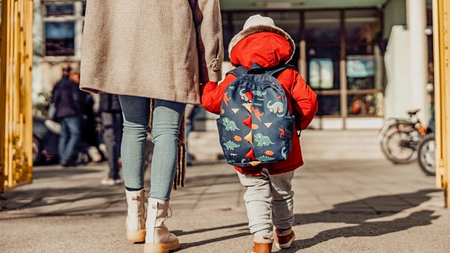 A kisd holding moms hand walking into school for a story on what to do when preschoolers cry at dropoff