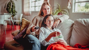 a middle schooler watchng tv with her mom on the couch