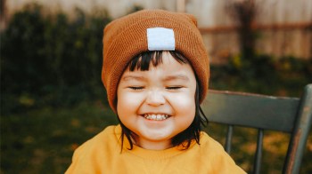 a little girl in a beanie hat smiling adorably before launching into some quirky toddler behavior