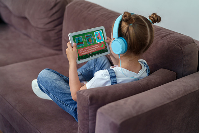 A young girl playing on the lingokids app on her couch