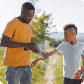 a dad spraying bug spray on his son to prevent mosquito bites