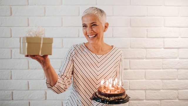 An older woman holding a gift and a cake to represent the latest baby trend, grandma showers