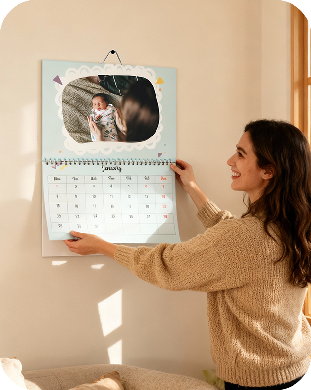 A woman hanging a calendar on the wall that she made in the tinybeans photo store
