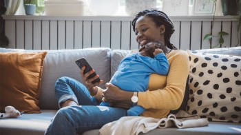 A mom entering baby journal prompts and milestones in her Tinybeans journal while her newborn sleeps on her chest