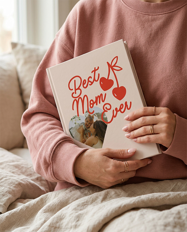 A woman holding a Tinybeans Mother's Day photo book that says Best Mom Ever with cherries and a photo
